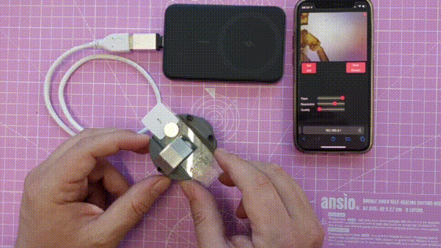 Hands adjusting the Matchboxscope while the image stream appears live on a smartphone screen